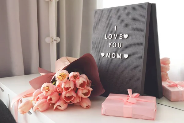 Beautiful tulips with the letter I LOVE MOM on letterboard sign. Pink background, frame, border. Lovely greeting card with tulips for Mothers day, wedding or happy event concepts.