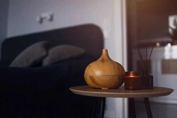 Aroma oil diffuser, air freshener and candle on a wooden table in the bedroom. Warm, atmospheric photography.