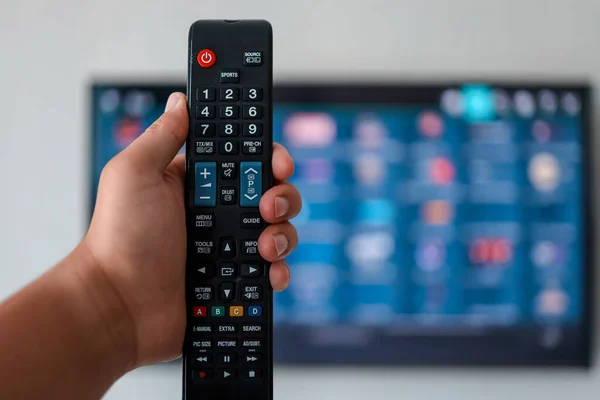 Smart tv and hand pressing remote control. Hand holding TV remote control with a television in the background. Close up.