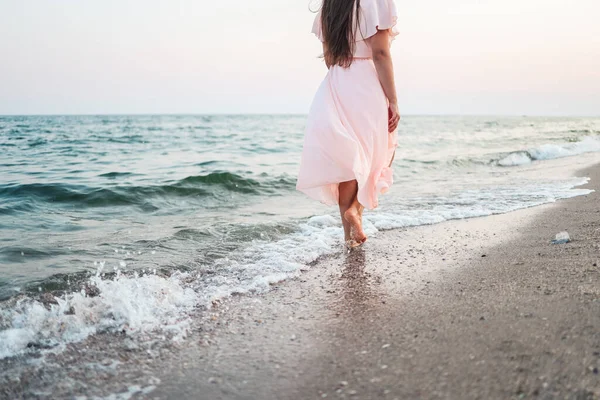 A girl in a pink dress runs along the seashore