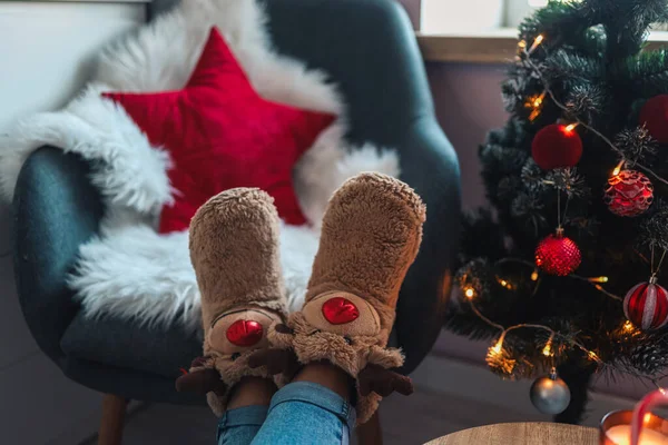 Feet in cute slippers on the background of the Christmas tree.