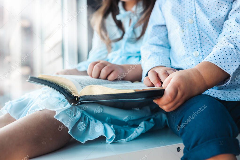 Two Little girl and boy hands folded in prayer on a Holy Bible together for faith concept.