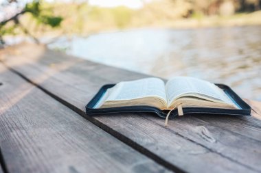 Open Bible on a wooden board near the river