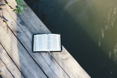 Open Bible on a wooden board near the river, top view, space for your text