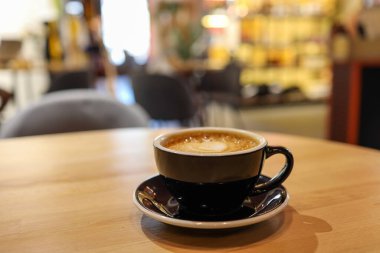 Coffee in black cup on wooden table in cafe with lighting background