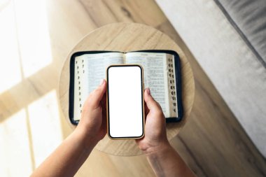 Woman hand hold and touch screen smart phone,cellphone in church over blurred bible holy and age book.