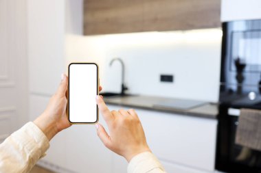 Kitchen background with hand with phone. Blurred home kitchen with blank smartphone screen. Online grocery ordering concept, online food shopping.