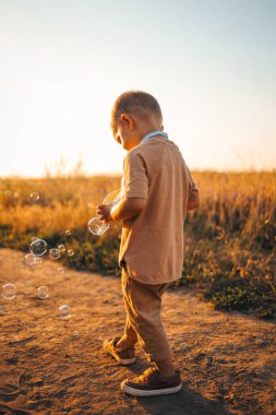 Little boy playing soap bubbles at sunset, happy carefree childhood.