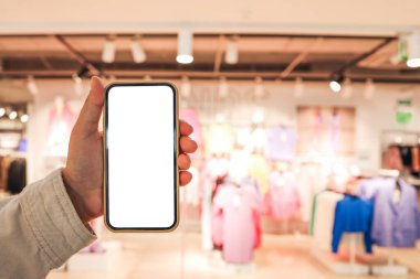 A girl holds a phone in her hand with a blank isolated screen on the background of a blurred shopping center.