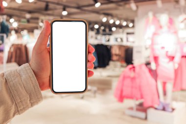 A girl holds a phone in her hand with a blank isolated screen on the background of a blurred shopping center.