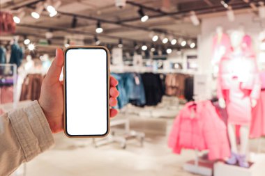 A girl holds a phone in her hand with a blank isolated screen on the background of a blurred shopping center.