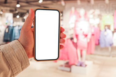 A girl holds a phone in her hand with a blank isolated screen on the background of a blurred shopping center.