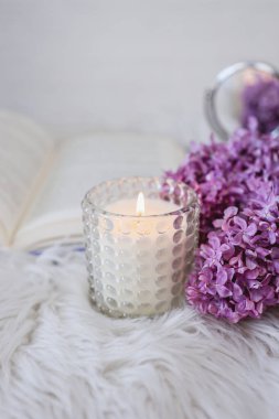 Beautiful candle close-up on the background of a book and lilacs.
