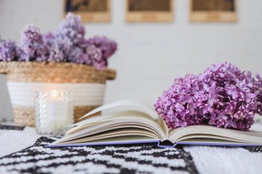 Wicker basket with lilacs, a candle, an open book on the table.Good morning concept.