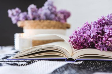 Wicker basket with lilacs, a candle, an open book on the table.Good morning concept.