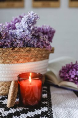 Wicker basket with lilacs, a candle, an open book on the table.Good morning concept.