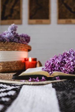 An open Bible with a lilac branch, a wicker basket and a candle on the table. Beautiful aesthetic good morning picture.