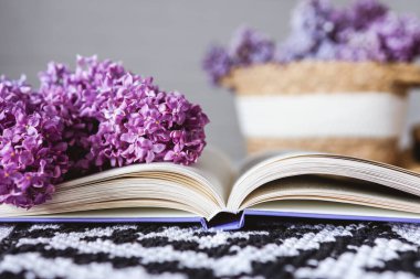 An open book with a lilac branch on a table with a wicker basket.