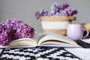 Wicker basket with lilacs, a candle, an open book on the table.Good morning concept.