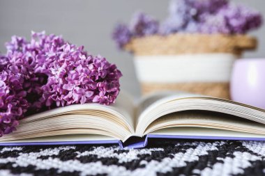 Wicker basket with lilacs, a candle, an open book on the table.Good morning concept.
