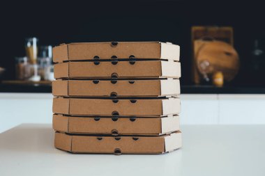 A stack of pizza boxes in the kitchen.