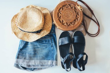 Black sandals, wicker hat, rattan bag and shorts, top view.
