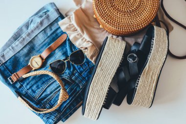 Women's summer clothes collage on white, flat lay. Woven sandals, rattan bag, watch, shorts, sunglasses top view.