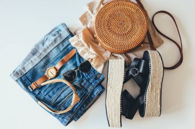 Women's summer clothes collage on white, flat lay. Woven sandals, rattan bag, watch, shorts, sunglasses top view.