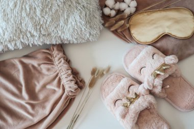 Açık arkaplanda ev terlikleri, uyku maskesi ve pijamaları olan düz bir kompozisyon.