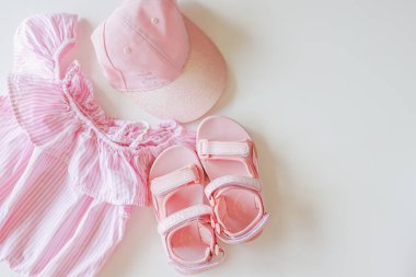 Set of children's clothes for girls in pink style. Sandals, cap and t-shirt, flat lay, top view.