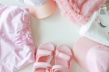 Set of children's clothes for girls in pink style. Sandals, cap and t-shirt, flat lay, top view.