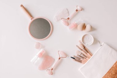 Bottles of cosmetic products, face roller and gua sha massager, mirror, cosmetic bag, brushes and sponge on a white isolated background. Banner. View from above. Spa vacation, body care, spa, skin care concept.
