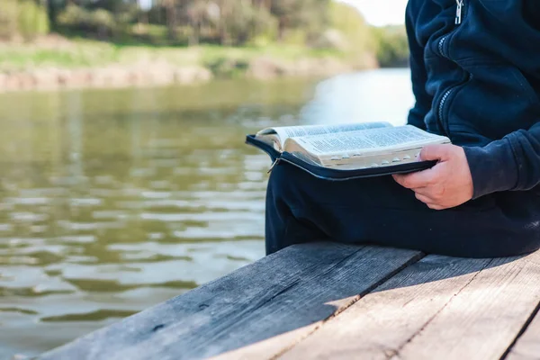 Child reads Bible book while sitting near pond. Christian illustration. Place for text.