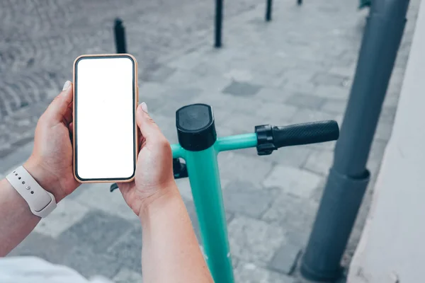 Girl standing with electric scooter and showing the phone with blank white screen