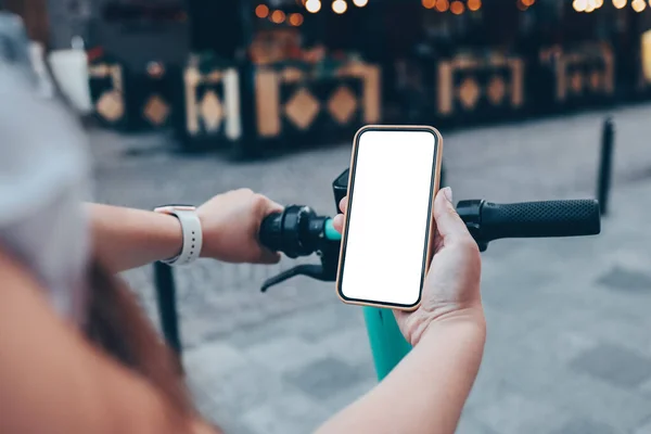 Girl standing with electric scooter and showing the phone with blank white screen