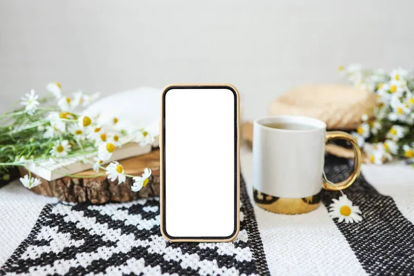 Phone screen with an isolated screen on the background of a cup of tea, a book and daisies, a place for your text