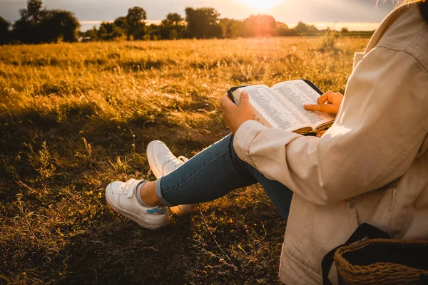 Christian woman holds bible in her hands. Reading the Holy Bible in a field during beautiful sunset. Concept for faith, spirituality and religion. Peace, hope