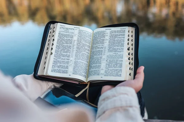 Girl reading the Bible on the river bank.