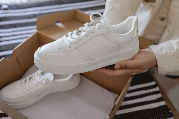 Unpacking women's shoes, stylish white sneakers in hands.