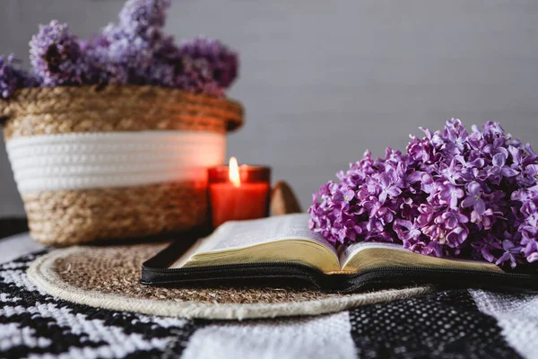 An open Bible with a lilac branch, a wicker basket and a candle on the table. Beautiful aesthetic good morning picture.