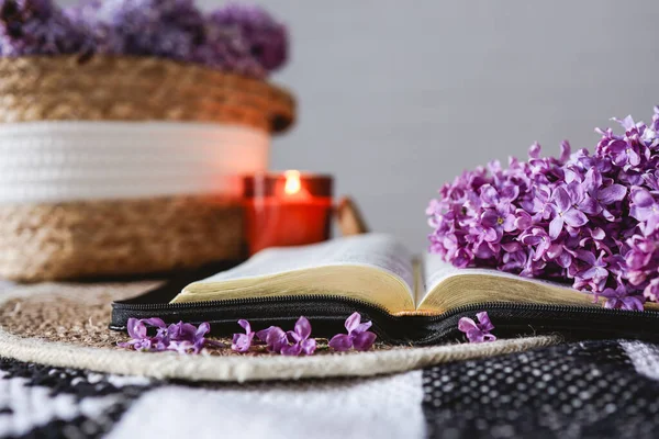 An open Bible with a lilac branch, a wicker basket and a candle on the table. Beautiful aesthetic good morning picture.
