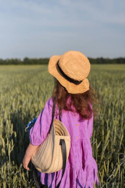 A girl in a hat walks through a field of wheat.