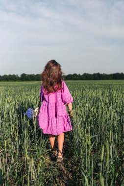 A girl in a hat walks through a field of wheat.