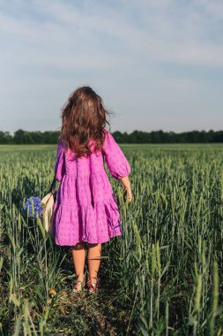 A girl in a hat walks through a field of wheat.
