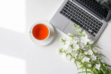 Siyah ekranlı dizüstü bilgisayarlı ofis masası, malzemeler, kahve ya da çay, beyaz masadaki çiçek buketi. İş kadını işyeri.