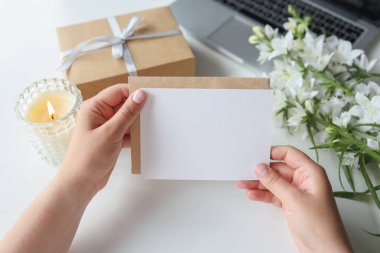 Woman holding envelope with blank greeting card, gift and flowers on the desktop