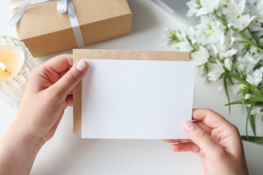 Woman holding envelope with blank greeting card, gift and flowers on the desktop