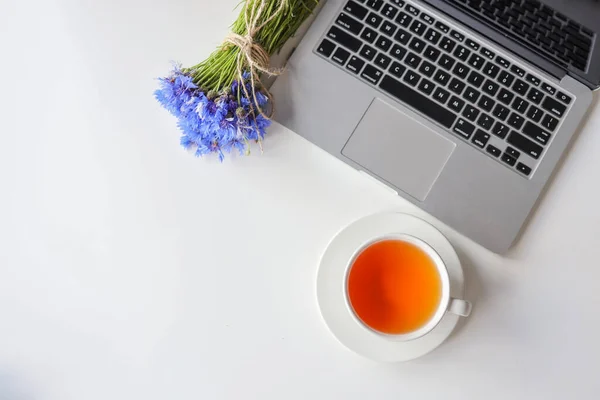 Office desk table with laptop computer with black screen, supplies, cup of coffee or tea, flowers bouquet on white table. Business woman workplace.