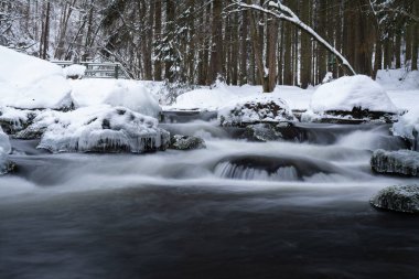Kışın nehirde kayaların ve kayaların üzerinde buz ve kayaların üzerinde ormanın güzel doğasında vahşi suyun yumuşak bir hareketi.