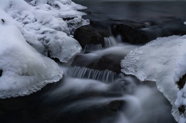 Kışın nehirde kayaların ve kayaların üzerinde buz ve kayaların üzerinde ormanın güzel doğasında vahşi suyun yumuşak bir hareketi.